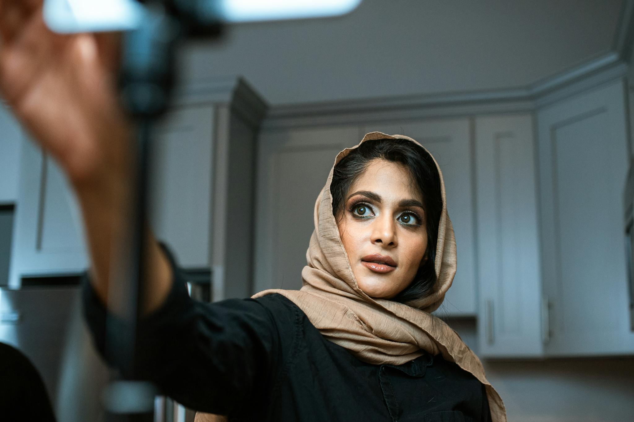 Woman in hijab recording a video on smartphone indoors, focusing on social media content creation.